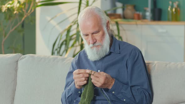 A Concentrated Elderly Man Knits While Sitting on a Sofa in His Cozy Living Room