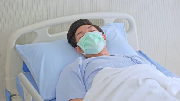 Asian male patient lying on bed with face mask to prevent covid19 in recovery room in hospital ward.