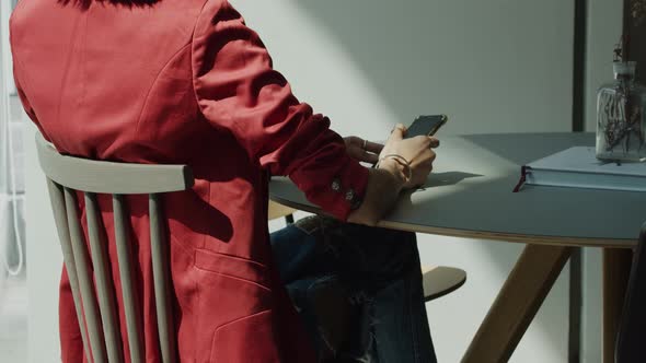 Woman, rear view, sitting at a table and text messaging or checking social media on a smartphone - c