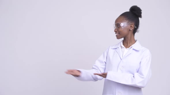 Young Happy African Woman Doctor with Protective Glasses Showing Something