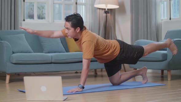 Asian Man On Mat Looking At A Laptop And Doing Yoga In Balancing Table Pose At Home