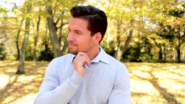 Young Handsome Man Stands in the Woods, Strokes His Chin, Looks Satisfied and Thinks About Something