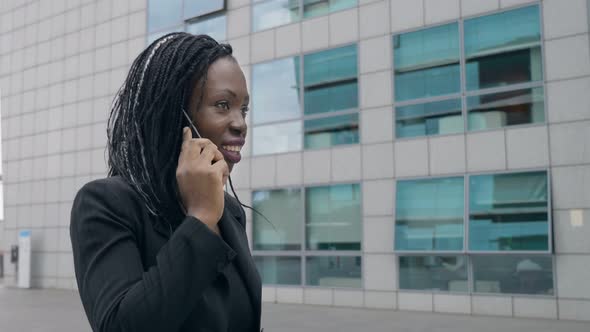 Confident successful black businesswoman talking by phone walking in the city