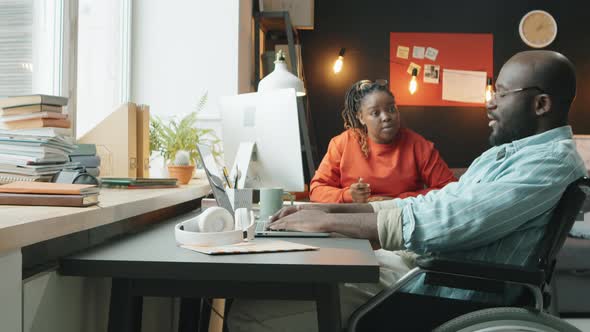 Man in Wheelchair Working on Laptop and Talking with Female Colleague