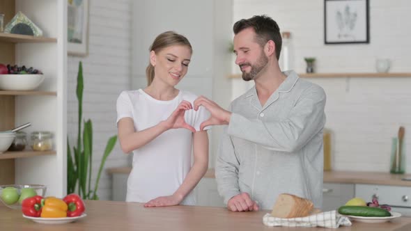 Happy Young Couple Making Heart Shape with Hands in Kitchen