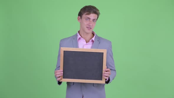 Happy Young Businessman Talking While Holding Blackboard