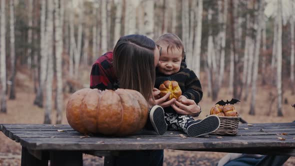 Young Woman and Her Baby Son in Autumn Park Boy Playing with Helloween Pumpkin and Eating Pumpkin