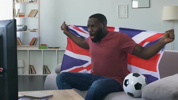 British Fan Cheering for National Team With Waving Flag, Watching Game at Home