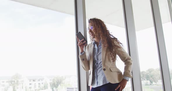 Biracial businesswoman smiling and talking on smartphone in modern interiors