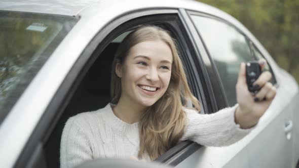 Closeup Portrait of Happy Young Beautiful Caucasian Woman Bragging Car Keys Sitting on Driver's Seat