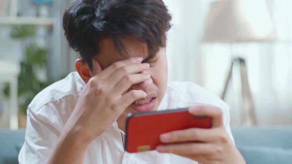 Close Up Of Asian Man Being Upset Losing Game On Smartphone While Sitting On Sofa In The Living Room