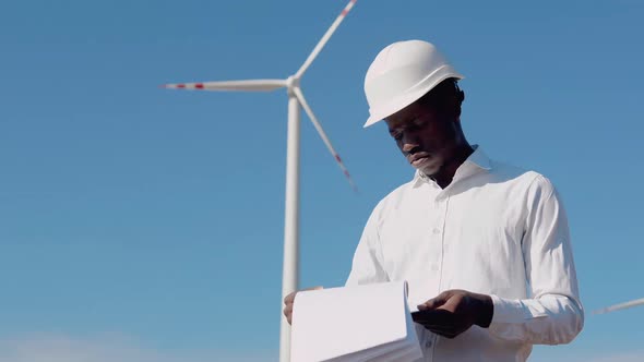African American Electrical Engineer Standing on the Background of a Windmill at an Air Power Plant