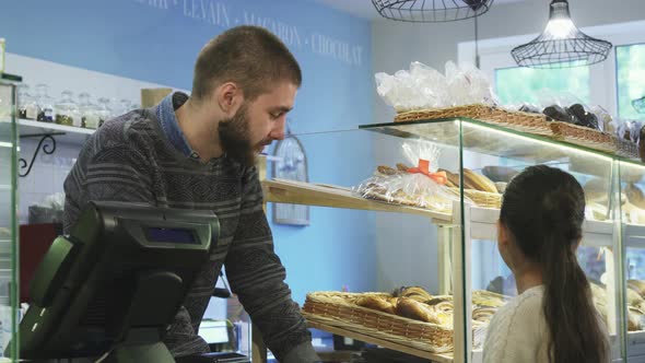 Young Male Baker Working at His Store Helping Little Girl Choosing Desserts