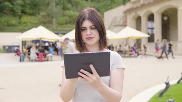 A Young Caucasian Woman Works on a Tablet in a City Park on a Sunny Day