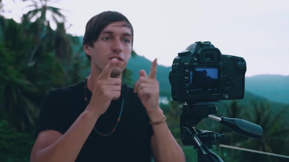 Young Man Blogger Talking to Camera Recording Video Blog Using a Professional Video Camera Mounted