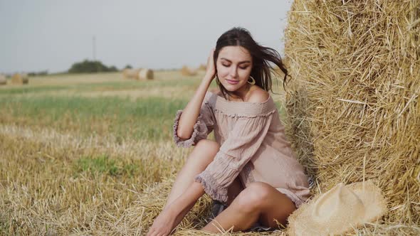 Lady in Dress Resting at a Haystack in a Field and Correcting Hair with Laugh