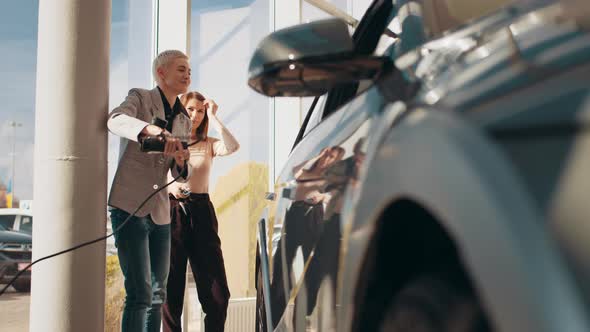 Two Beautiful Women Friends in Business Suit Standing in Electric Car Dealership