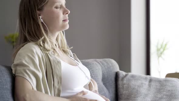 Calm Pregnant Woman Enjoying Music and Massaging Belly