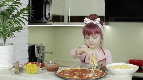 Cooking Pizza. Little Child in Apron Adding Grated Cheese To Dough in Kitchen