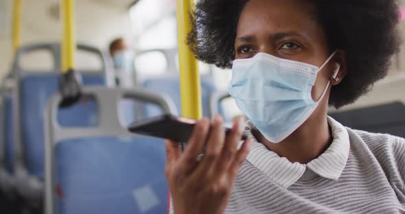 African american businesswoman with face mask talking on smartphone and sitting in bus