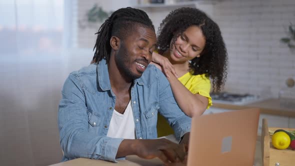 Positive Handsome African American Man Closing Laptop and Talking with Loving Woman in Kitchen at