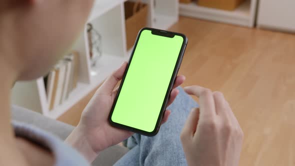 handle shot of woman holding mockup smartphone green screen on the sofa at home.