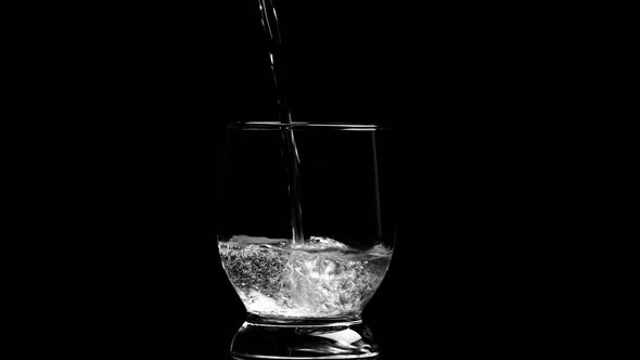 water with gurgles is poured into a glass on a black background