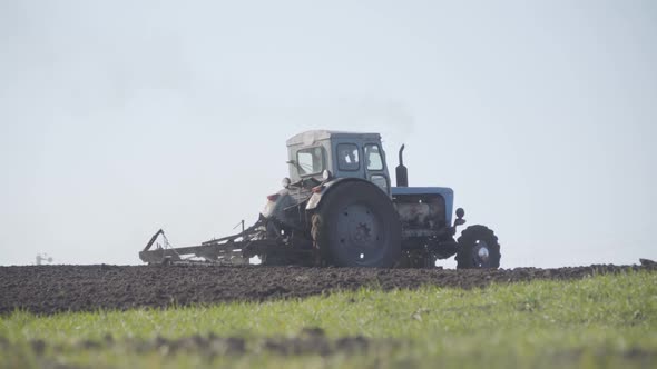 Wide Shot of Old Tractor Furrowing Agricultural Field. Engineering Vehicle Cultivating Soil on Sunny