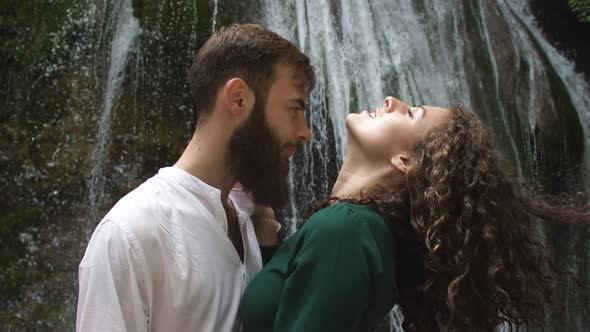 Sexy Young Woman with Curly Blond Hair in the Arms of a Young Man with a Beard on the Background of