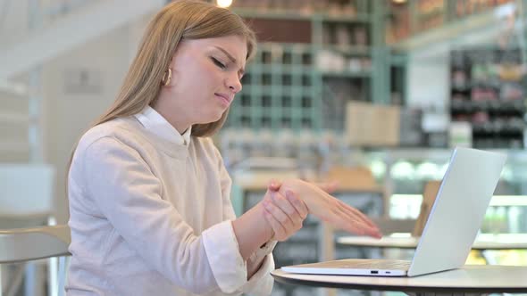 Young Woman with Wrist Pain Using Laptop in Cafe