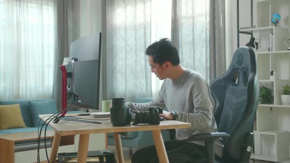 Asian Cameraman Looking At Desktop Computer And Writing In Notebook On A Table While Working At Home
