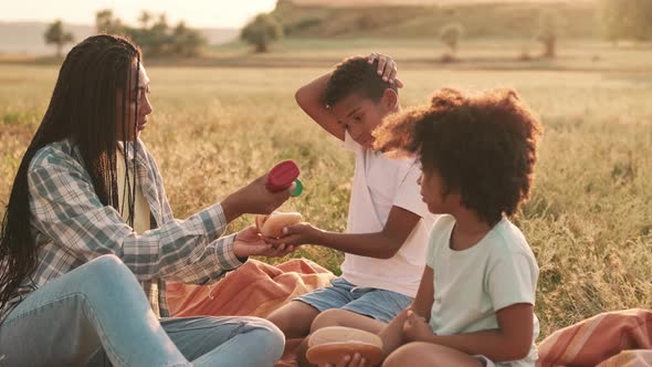 A good-looking afro-american mother and her children are eating hot-dogs