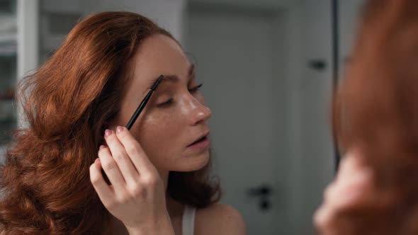 Caucasian woman brushing eyebrows in the mirror reflection. Shot with RED helium camera in 4K.