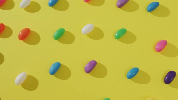 Video of overhead view of rows of multi coloured sweets over yellow background