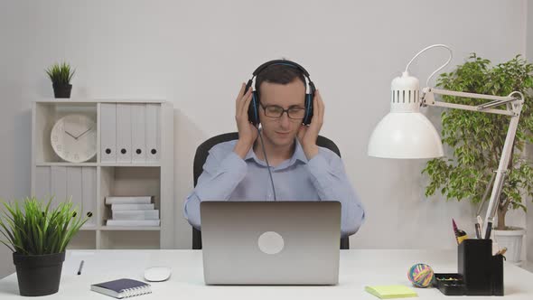 Relaxed Businessman Singing and Listening Music Using Headphones at Office