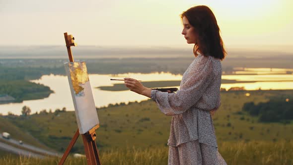 Young Smiling Woman Drawing a Painting on Nature Standing on the Field While Sunset