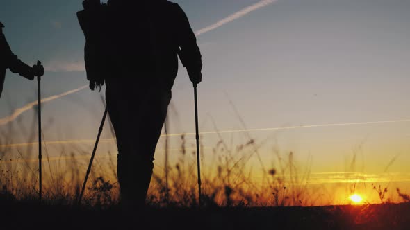 Silhouettes of Two Hikers with Backpacks Enjoying Sunset View From Top of a Mountain. Enjoying the