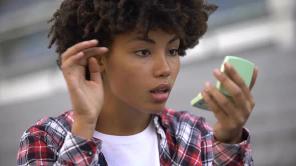 Attractive Young Woman Adjusting Her Make-Up, Looking in Hand Mirror Outdoors