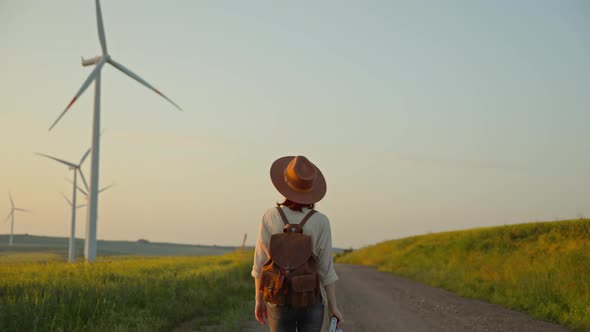 Young photographer with a camera walking near a field with alternative green energy windmills