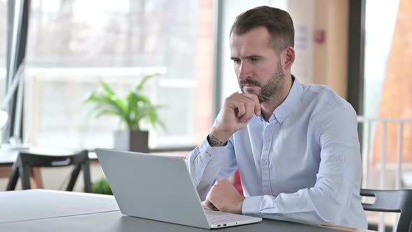 Thoughtful Young Man Working on Laptop in Office