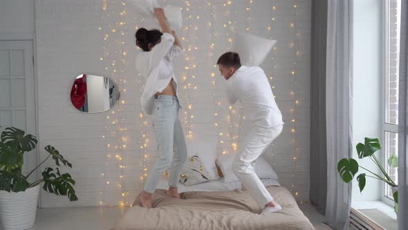 Young Beautiful Loving Couple Fight Together with Pillows on the Bed