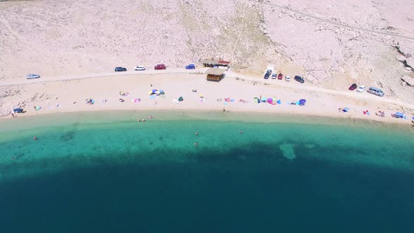 Flying above umbrellas and people on isolated beach of Pag island, Croatia