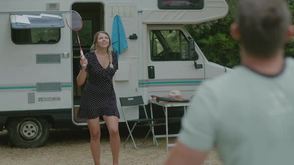 Happy traveler man and woman play badminton together in nature enjoyng vacation near motor home