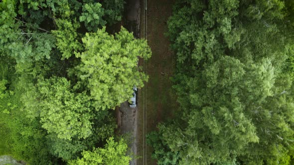 Top view drone follows black car driving along highway in cloudy autumn forest on road trip