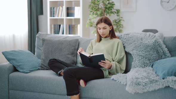 Woman Sitting on Couch and Reading Book