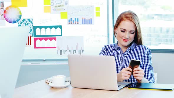 Beautiful female graphic designer using mobile phone in conference room