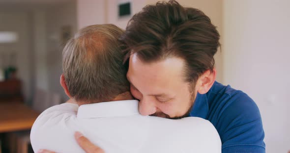 A Smiling Young Man Hugs His Elderly Father at Home