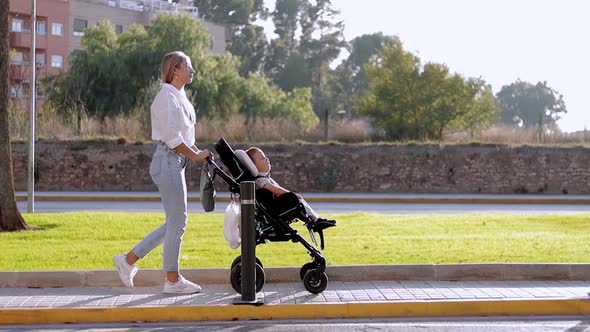 Video of Family Mother Walking Outdoors and Carer Helping Look at Disabled Son Child Sitting in