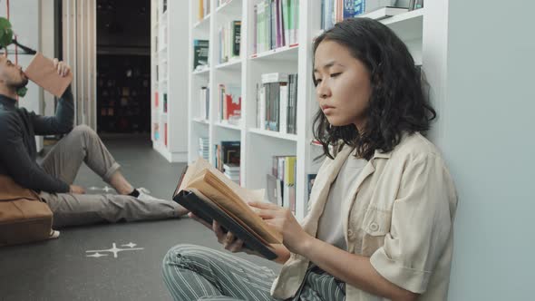 Asian Woman Reading on Floor in Library