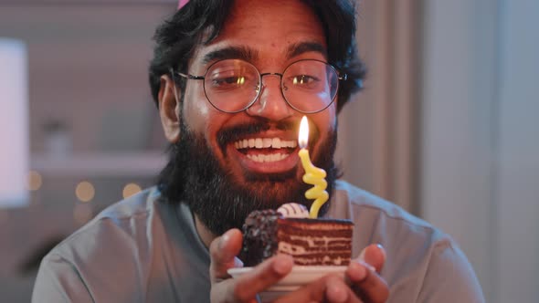 Portrait of Multiracial Man with Thick Black Beard in Glasses and Festive Hat with Cake in Light in